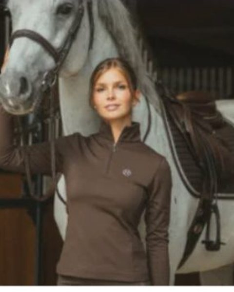 A rider in Harcour training wear beside a gray horse in the stables — the equipment prize of the EquiAction charity lottery.