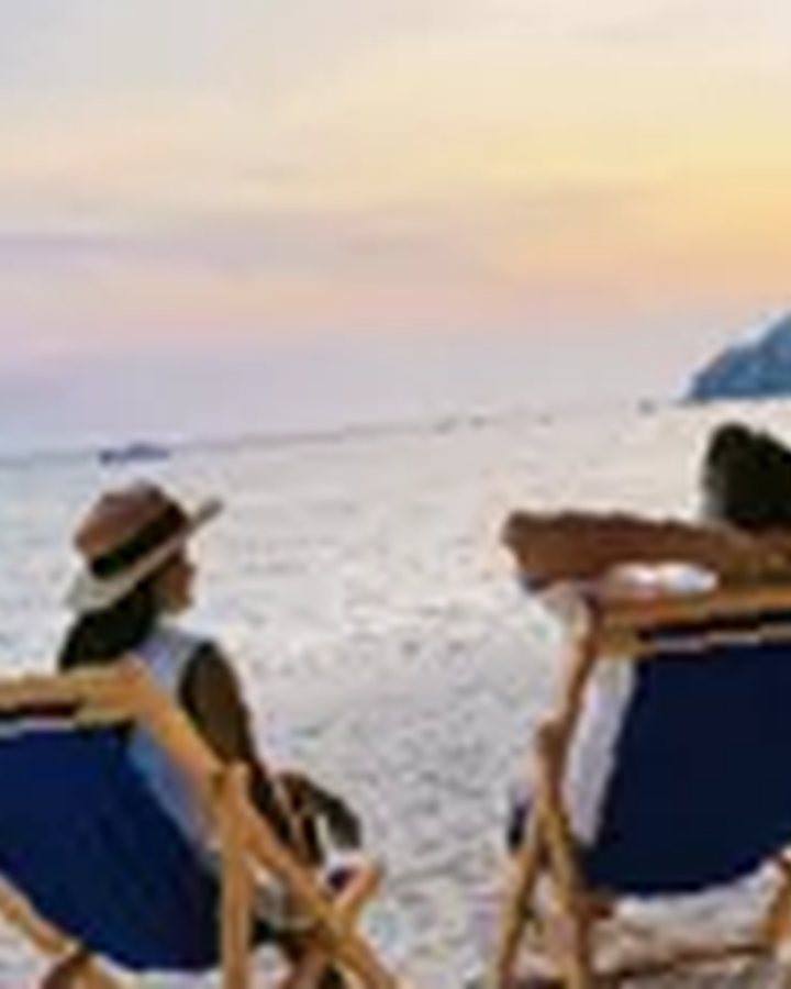 Réunion: two people in deck chairs facing the ocean at sunset, on a fine sand beach, pink and golden sky