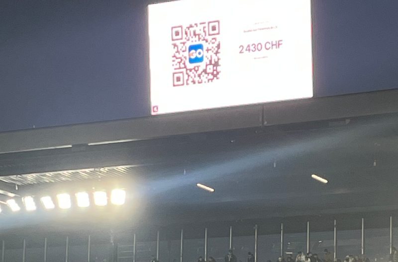 The big screen of a Super League stadium showing the Live Wall counter of Le Papet du LS and its QR code (2 430 CHF live), above the Kop Sud stand.
