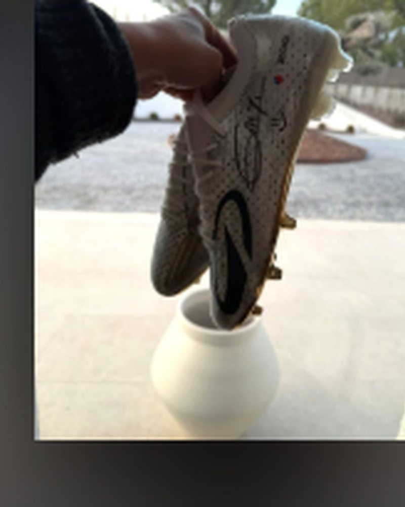 Pair of limited-edition football boots signed by Antoine Griezmann, held up in front of a stadium