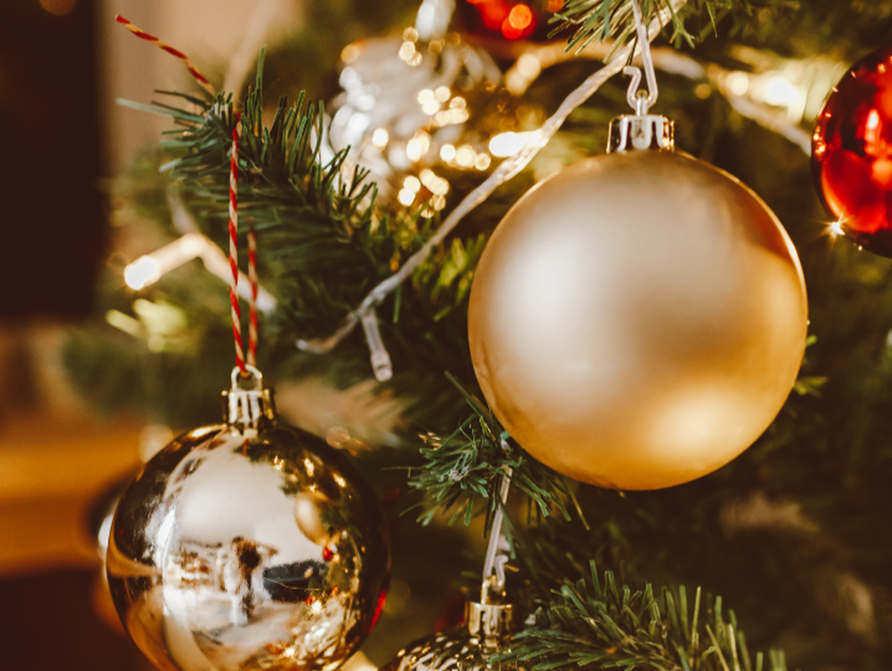 Primo piano di palline di Natale dorate e argentate appese a un albero con una catena di luci