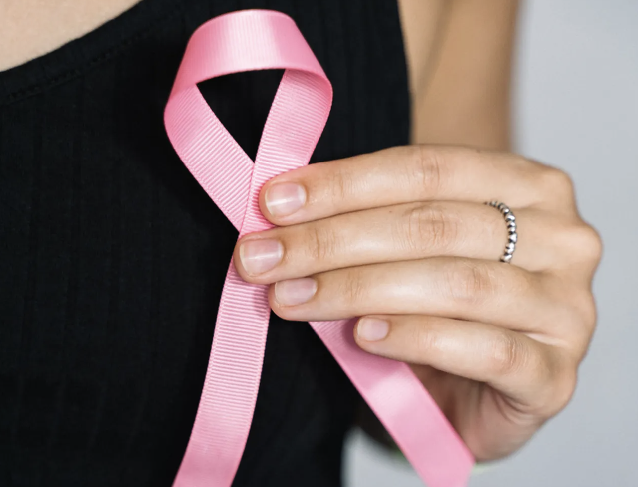 Nahaufnahme einer Hand, die eine rosa Brustkrebs-Schleife vor einem schwarzen Oberteil hält