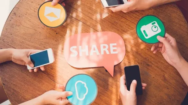 Top view of a round table where four people, smartphones in hand, surround a speech bubble reading SHARE.
